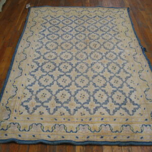 Off-white rug with blue geometric lattice and yellow motifs, bordered in blue, covers a wood floor.