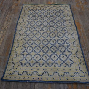 Textured pale yellow rug featuring a repeating blue geometric lattice pattern on dark, distressed wood planks.
