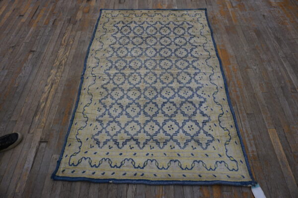 Textured pale yellow rug featuring a repeating blue geometric lattice pattern on dark, distressed wood planks.