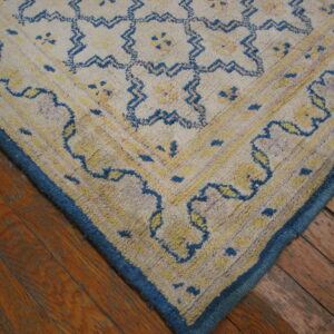Shaggy cream rug corner with blue and yellow geometric patterns and a solid blue border on wood planks.