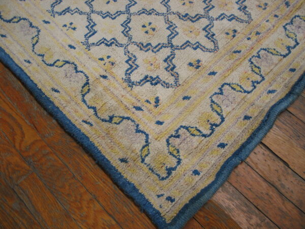 Shaggy cream rug corner with blue and yellow geometric patterns and a solid blue border on wood planks.