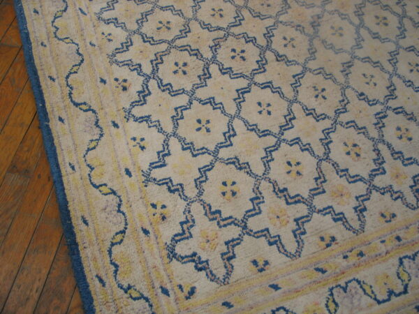 Beige high-pile rug with blue geometric lattice and yellow motifs on wood plank flooring.
