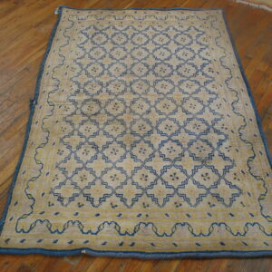 A beige rug with a blue and yellow geometric lattice pattern lies on distressed wood flooring.
