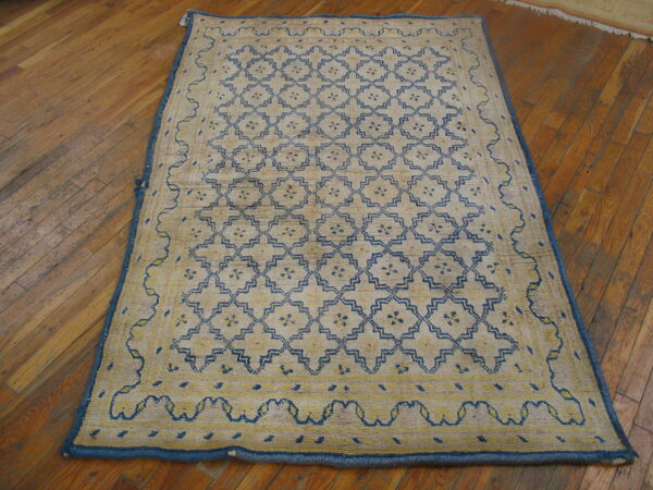 A beige rug with a blue and yellow geometric lattice pattern lies on distressed wood flooring.