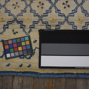 Close-up of a textured cream and dark blue geometric rug on wood, including calibration tools.