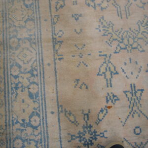 Close-up of a faded pink and cream rug featuring distressed blue geometric and stick figure patterns on wood flooring.