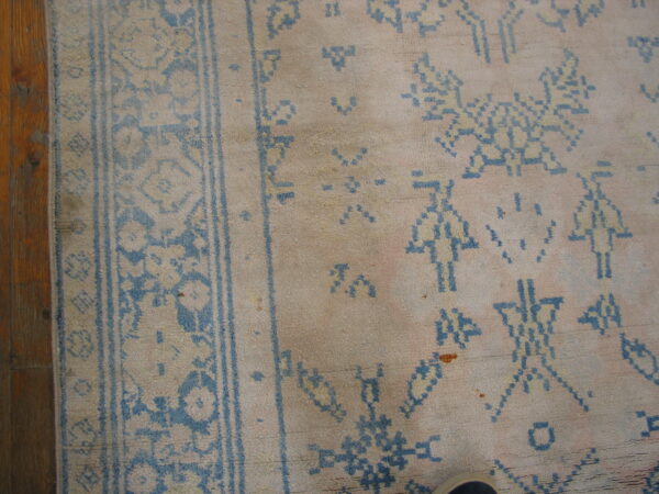 Close-up of a faded pink and cream rug featuring distressed blue geometric and stick figure patterns on wood flooring.