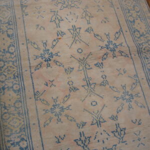 Low-pile runner with pale pink and beige field colors, featuring blue geometric symbols on wood flooring.