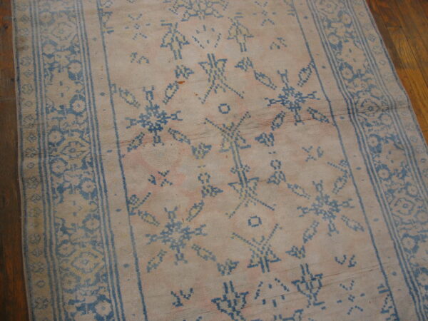 Low-pile runner with pale pink and beige field colors, featuring blue geometric symbols on wood flooring.