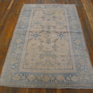 Light blue and tan distressed rug featuring a central medallion and multiple borders on glossy wood floors.