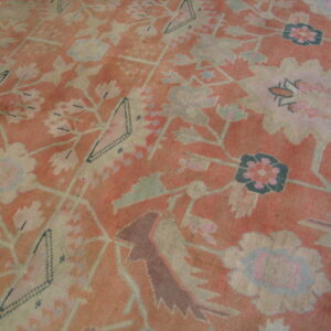 Faded coral rug featuring large stylized flowers and geometric diamonds in pale green and cream.