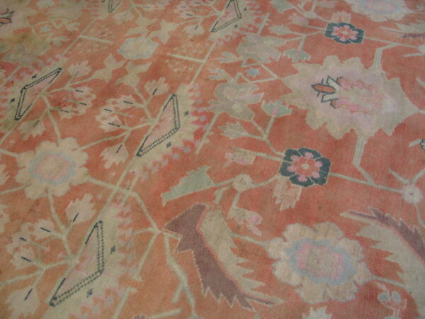 Faded coral rug featuring large stylized flowers and geometric diamonds in pale green and cream.
