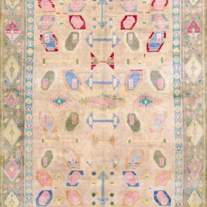 This rug displays geometric abstract shapes in pastel pink, blue, red, and olive green on a light beige field.