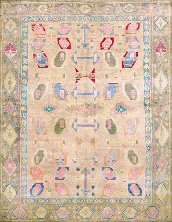 This rug displays geometric abstract shapes in pastel pink, blue, red, and olive green on a light beige field.