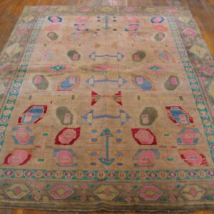 Distressed rug featuring large abstract motifs in bright pink, blue, and olive green on wood flooring.