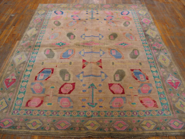 Distressed rug featuring large abstract motifs in bright pink, blue, and olive green on wood flooring.