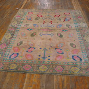 Distressed beige rug with colorful geometric motifs in pink, blue, and teal on wide wood plank flooring.