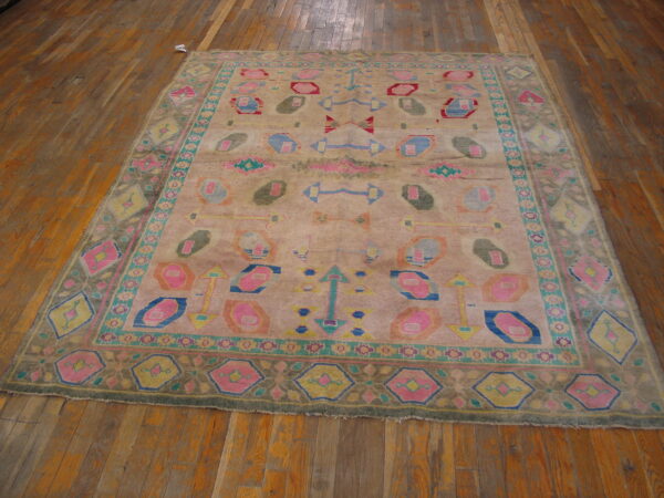 Distressed beige rug with colorful geometric motifs in pink, blue, and teal on wide wood plank flooring.