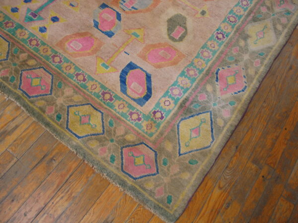 Geometric rug with bright pink and blue designs on a tan ground lies on rustic wooden flooring.