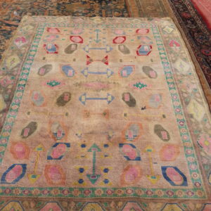 Faded pink and tan rug featuring brightly colored geometric and abstract motifs layered on other rugs.