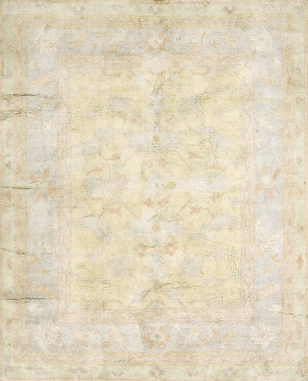 Low pile rug featuring a muted and distressed traditional pattern in beige, yellow, and pastel blue.