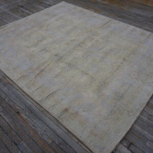 A textured beige and gray rug with a faint geometric pattern sits on rustic dark wood planks.