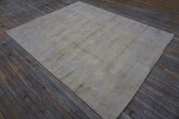 A textured beige and gray rug with a faint geometric pattern sits on rustic dark wood planks.