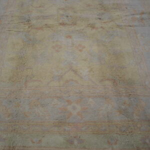 Muted gray and beige high-pile rug with faint pink traditional patterns on a dark wood floor.