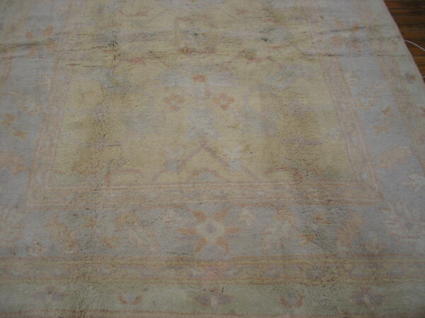 Muted gray and beige high-pile rug with faint pink traditional patterns on a dark wood floor.