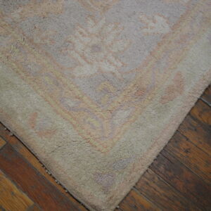 Close-up of a high pile rug in muted pastels and beige on a dark, distressed hardwood floor.