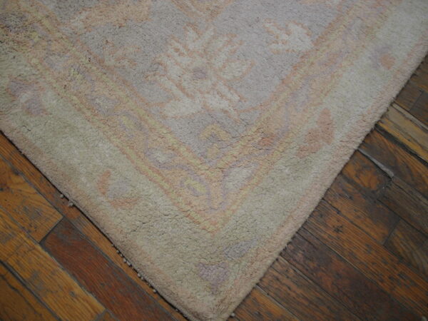 Close-up of a high pile rug in muted pastels and beige on a dark, distressed hardwood floor.