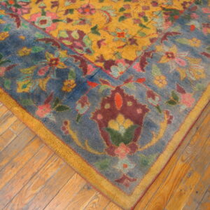 Multicolored floral rug with a yellow field and dusty blue border lying on worn wood floors.