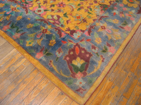 Multicolored floral rug with a yellow field and dusty blue border lying on worn wood floors.