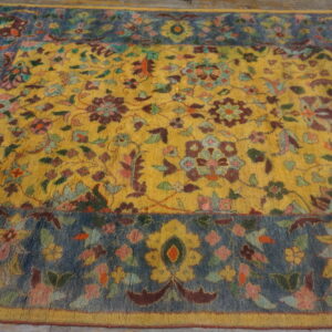 Colorful high-pile rug with a detailed yellow floral field and a contrasting blue patterned border on wood floor.