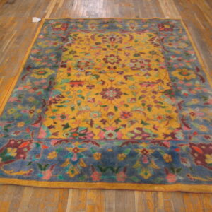 Ornate rug with a golden yellow center, multicolored floral pattern, and dusty blue border on hardwood floors.