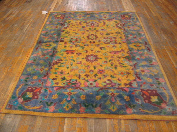 Ornate rug with a golden yellow center, multicolored floral pattern, and dusty blue border on hardwood floors.