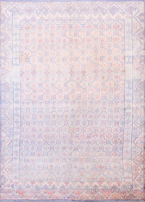 Low-pile rug with a repeating geometric and floral pattern in faded cream, light blue, and pink.