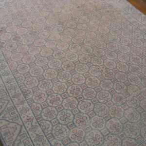 Distressed rug featuring repeating pink and blue geometric medallions set on hardwood flooring.