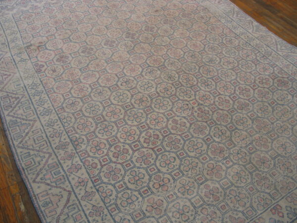 Distressed rug featuring repeating pink and blue geometric medallions set on hardwood flooring.