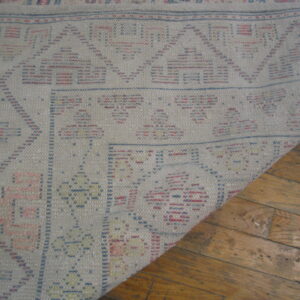 Geometric gray flatwoven rug with blue and pink patterns curled back from rustic wood floors.