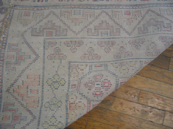 Geometric gray flatwoven rug with blue and pink patterns curled back from rustic wood floors.