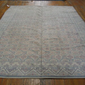 Large, low-pile rug with a geometric trellis pattern in faded blue and pink on wooden flooring.