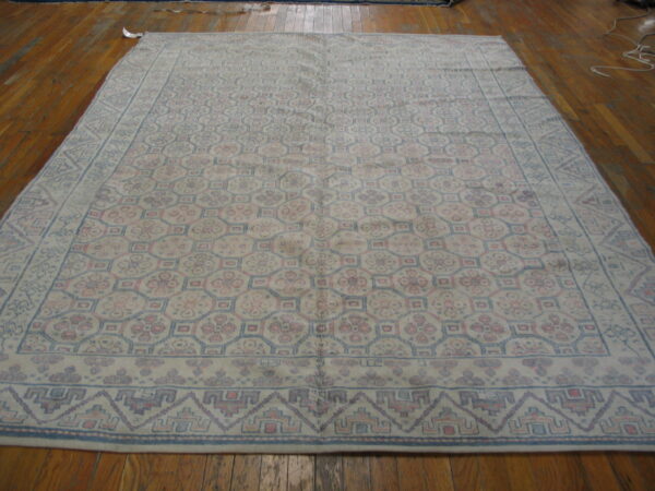 Large, low-pile rug with a geometric trellis pattern in faded blue and pink on wooden flooring.