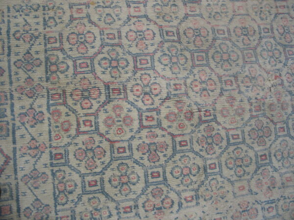 Muted geometric lattice rug in beige, dusty blue, and pink with visible distressed pile texture.