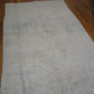 Distressed light gray and blue textured rug on hardwood planks, with a second patterned rug visible nearby.