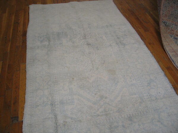 Distressed light gray and blue textured rug on hardwood planks, with a second patterned rug visible nearby.