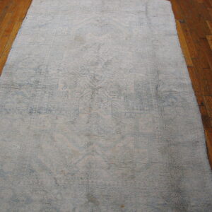 Shaggy light gray and faded blue patterned runner rug rests on warm brown hardwood flooring.