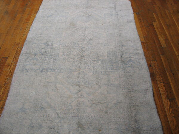 Shaggy light gray and faded blue patterned runner rug rests on warm brown hardwood flooring.