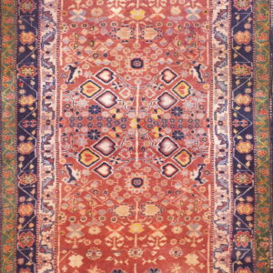Rust-colored traditional rug with layered navy and green borders and detailed geometric motifs.