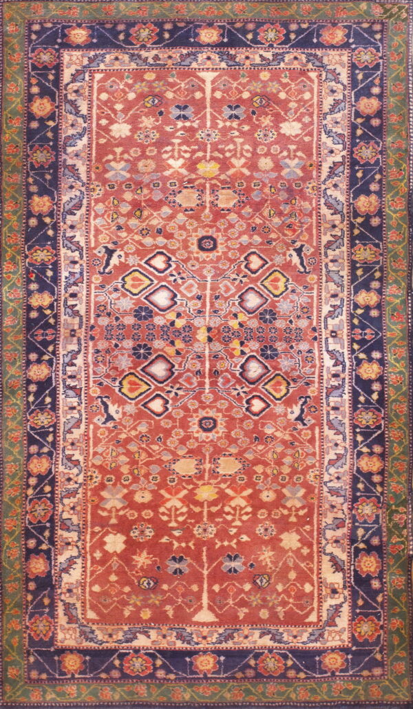 Rust-colored traditional rug with layered navy and green borders and detailed geometric motifs.